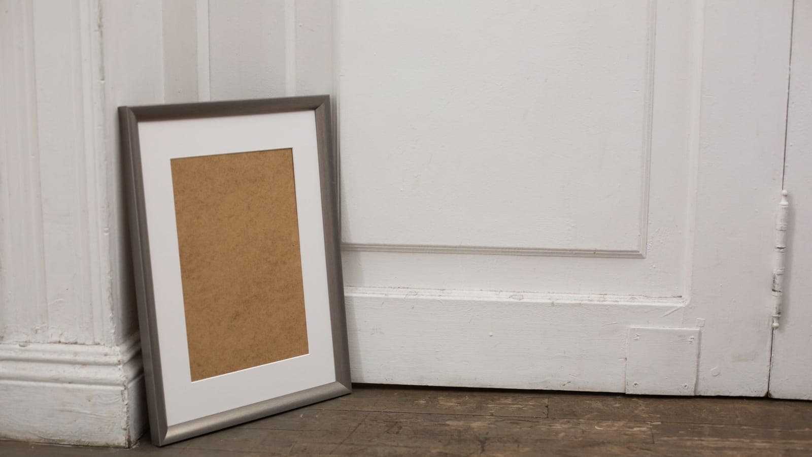 Simple frame placed on timber floor near white door in apartment with minimal design
