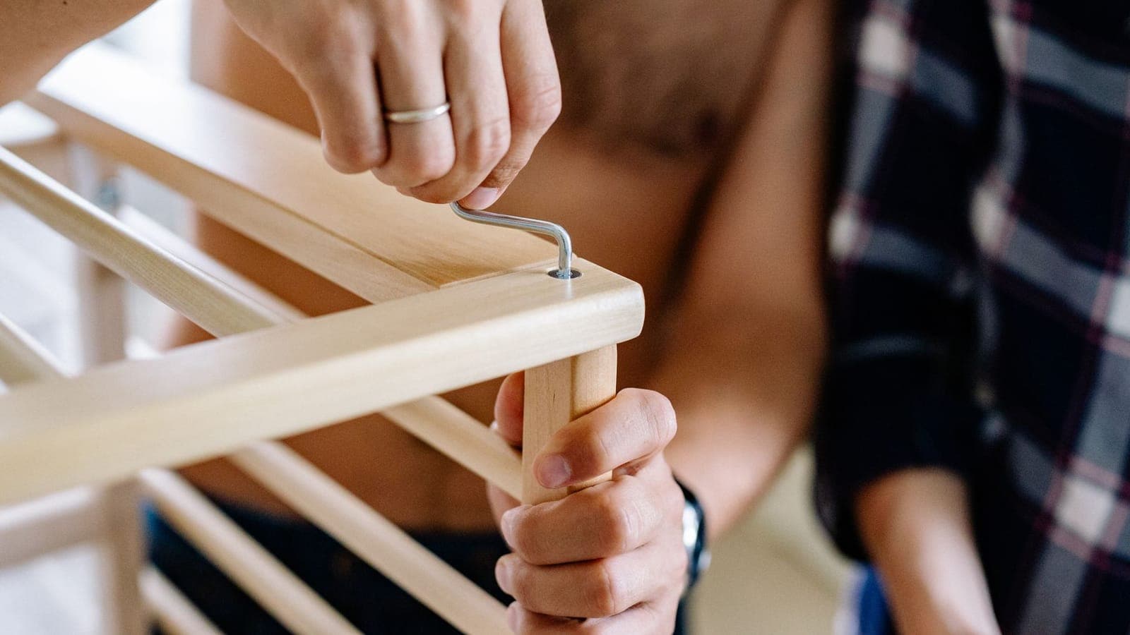 Close-up of a couple working together to assemble a wooden crib indoors.